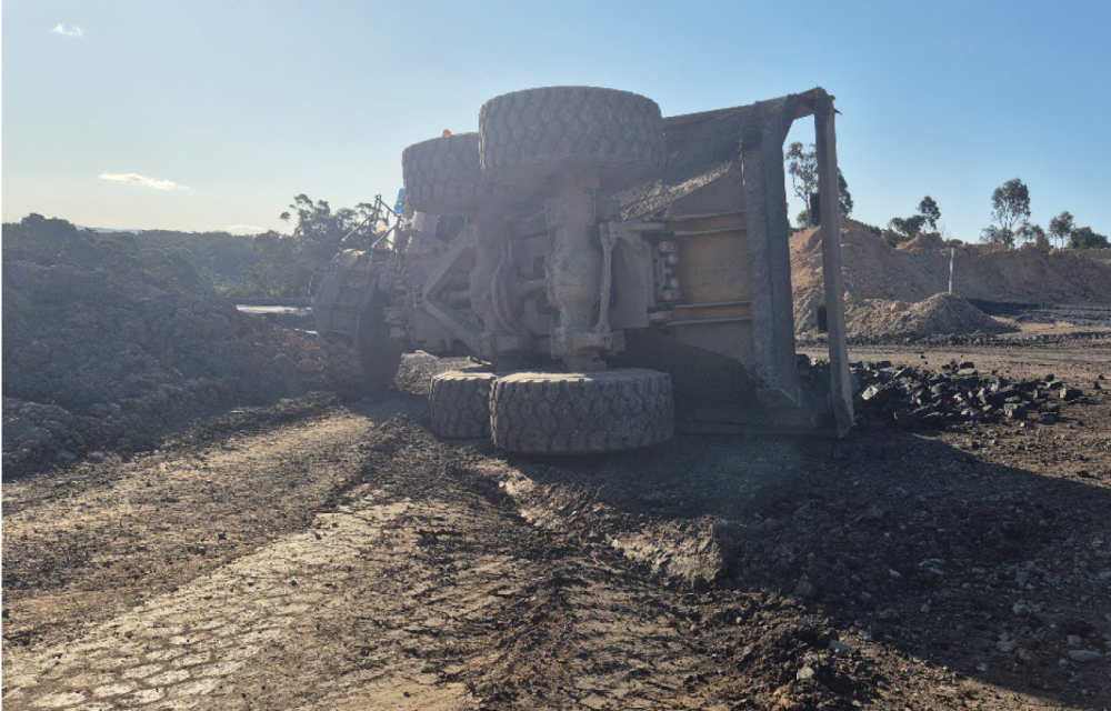 Haul truck rollover scene showing tub tipped after reversing into windrow, highlighting vehicle stability risks and poor ground conditions.