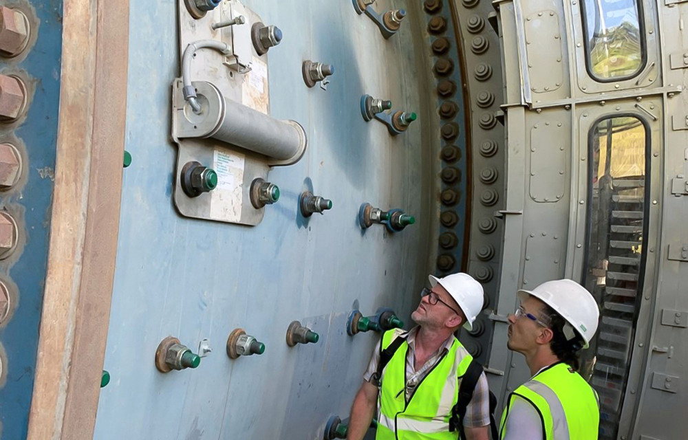 Engineers inspect a smart sensor installed on a grinding mill used to monitor and optimise particle size in real time for improved mineral processing performance.